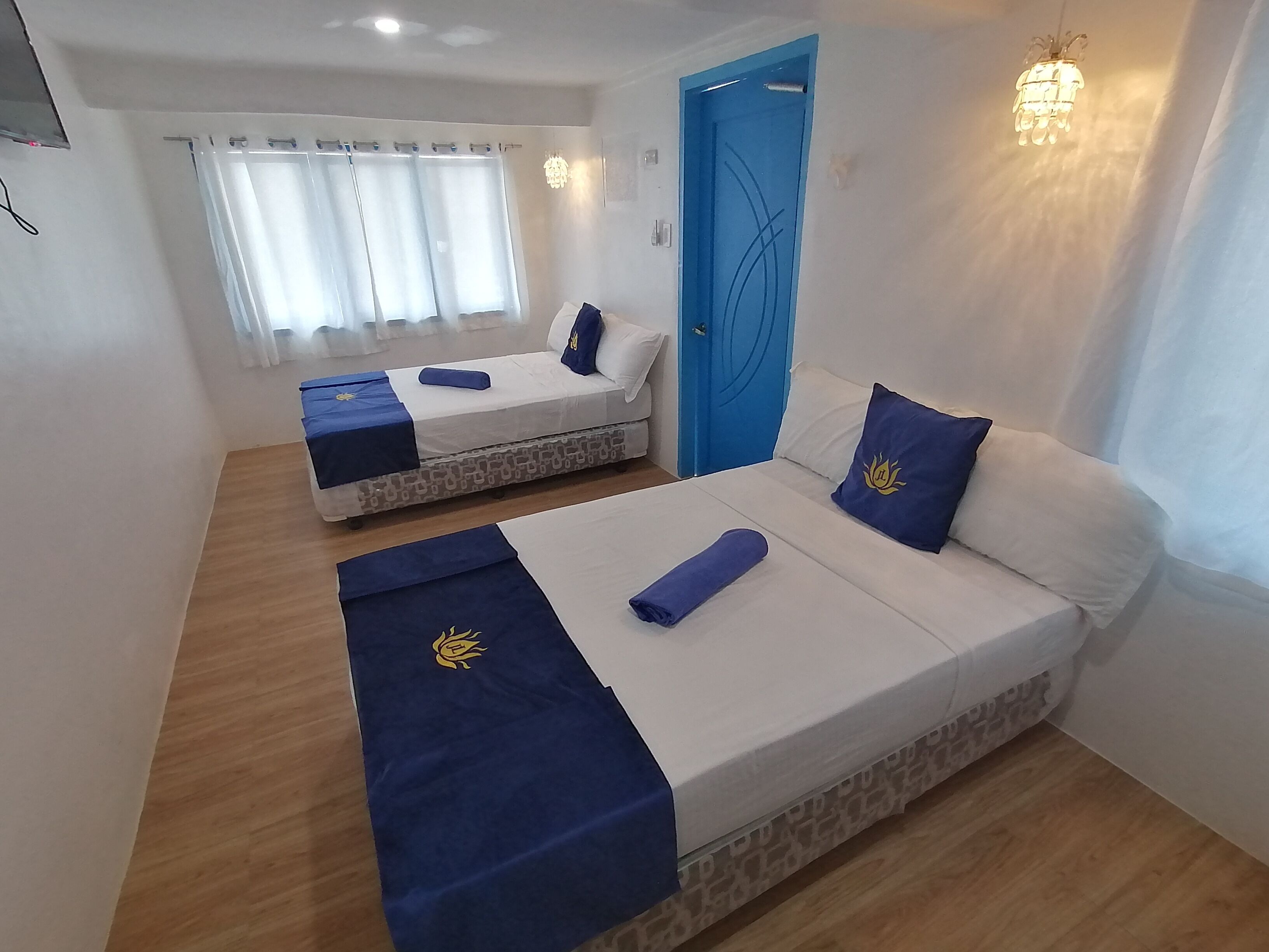 A hotel room with two beds, a blue door, and a window with curtains.
