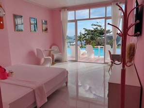 Une chambre d’hôtel décorée dans des tons roses, comprenant un lit, deux chaises, une petite table et une vue sur une piscine et l’océan.