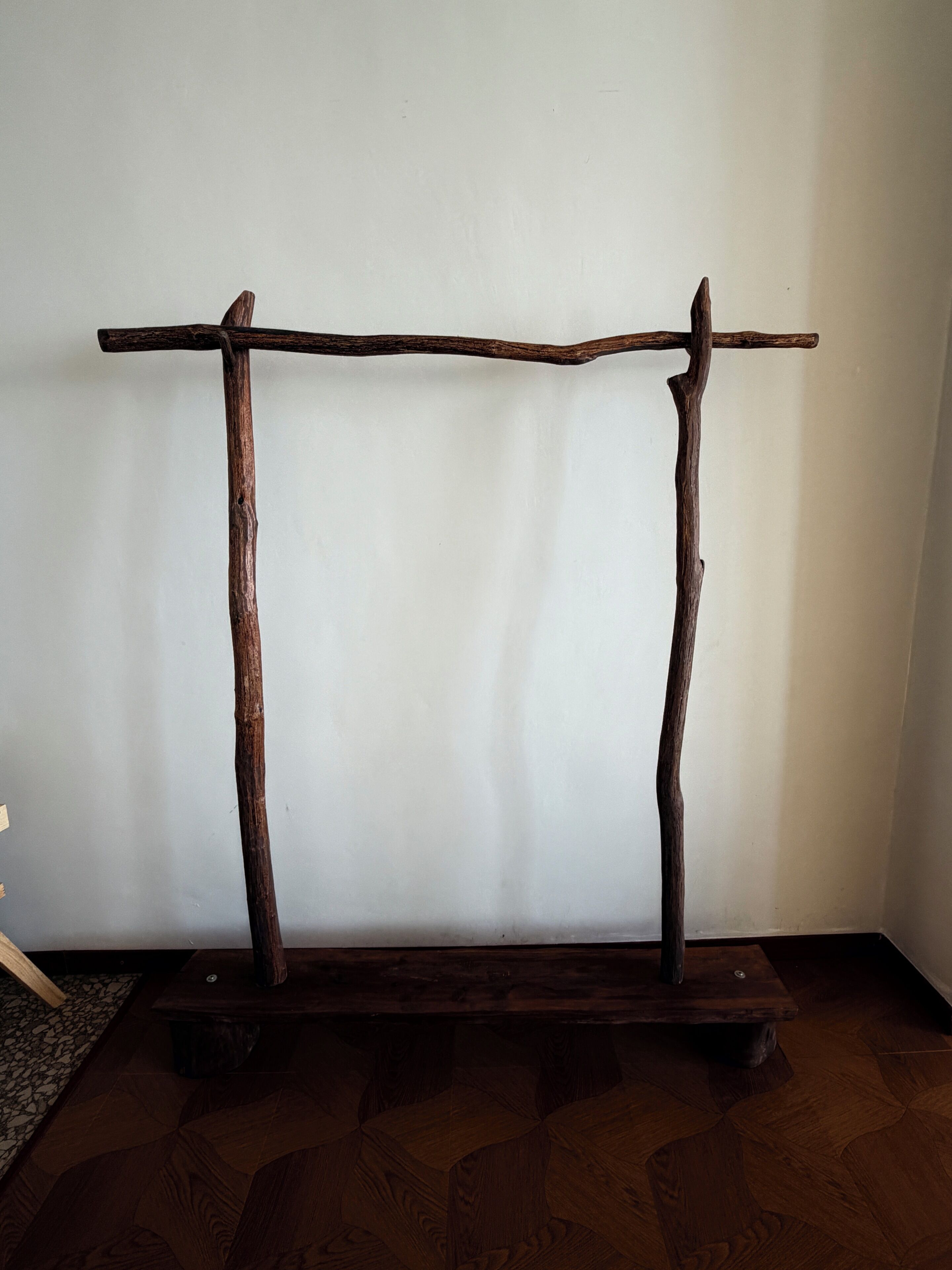 A rustic wooden bench with a simple design, placed against a plain wall.