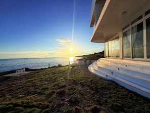 Un edificio moderno con fachada de vidrio que domina un paisaje costero durante el atardecer.