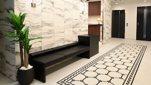 A modern lobby with marble walls, a black bench, a potted plant, and a geometric-patterned carpet. - Amistad Hotel Fukuoka (Fukuoka)