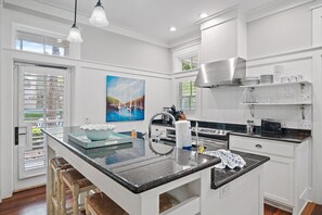 A modern kitchen with a central island, white cabinetry, and a painting above the sink. - Huge at 2,360 SqFt, Golf Cart & 4 Bikes! 4 WaterColor Pools, Beach Club & Camp - Bess Place on Earth (Santa Rosa Beach)