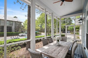 A covered outdoor seating area with a table and chairs, overlooking a street and greenery. - Huge at 2,360 SqFt, Golf Cart & 4 Bikes! 4 WaterColor Pools, Beach Club & Camp - Bess Place on Earth (Santa Rosa Beach)