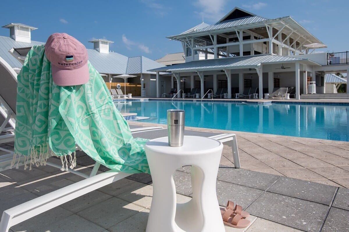 A poolside area with lounge chairs, a covered seating area, and a building with a modern architectural style.