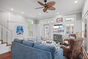 A living room with a blue sofa, wicker chairs, a ceiling fan, and a TV on a cabinet. - Huge at 2,360 SqFt, Golf Cart & 4 Bikes! 4 WaterColor Pools, Beach Club & Camp - Bess Place on Earth (Santa Rosa Beach)