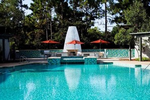 Una piscina con una fuente central, rodeada de sillas de descanso y sombrillas rojas.