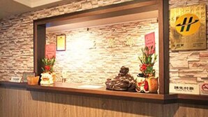 A reception desk with a stone wall backdrop, a framed sign with a symbol, and two potted plants. - Ya Tai Hotel (Kaohsiung)