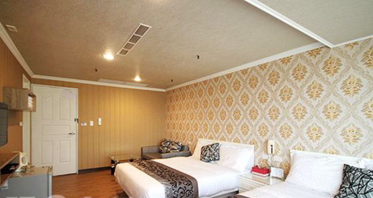 A hotel room with a bed, bedside tables, a wardrobe, and a patterned wallpaper.