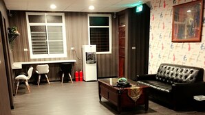 A spacious room with a wooden floor, a sofa, a coffee table, a desk with a chair, and a water dispenser. - Ya Tai Hotel (Kaohsiung)