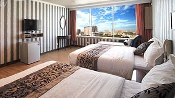 A hotel room with two beds, a TV, a small fridge, and a view of the city.