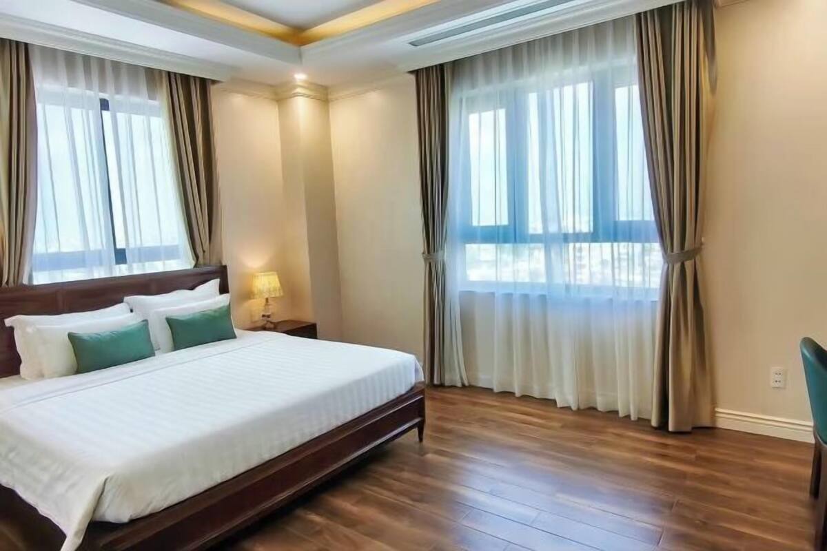 Une chambre d’hôtel avec un grand lit, un plancher en bois et des rideaux aux fenêtres.