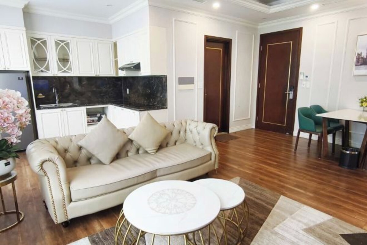 A living room with a beige sofa, two white round tables, and a kitchen area with white cabinets and a black countertop.