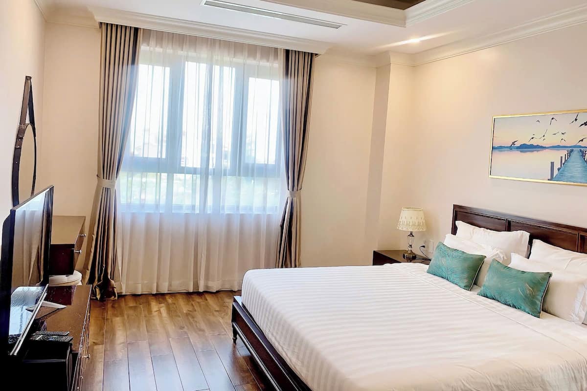 Une chambre d’hôtel avec un grand lit, une télévision, un bureau et une fenêtre avec des rideaux.