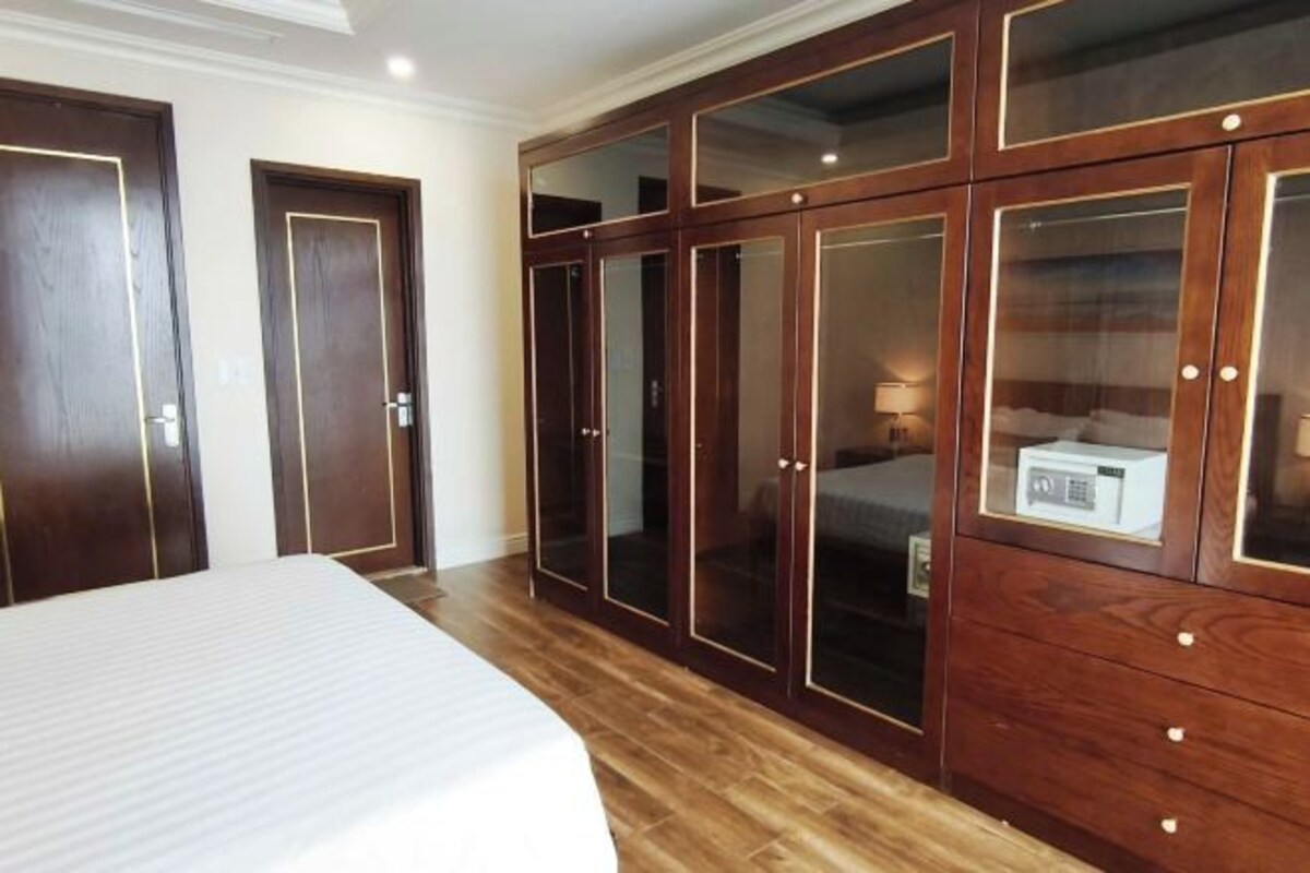 A bedroom with a large bed, wooden wardrobe with glass doors, and a bedside table with a lamp.