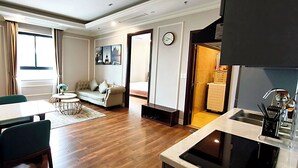 Una sala moderna con sofá, mesa de comedor y sillas, una cocina con fregadero y estufa, y un amplio ventanal con cortinas.