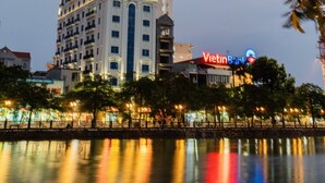 Un hotel de varios pisos con un llamativo letrero de 'Vietnam Bank' que se refleja en un cuerpo de agua tranquilo.