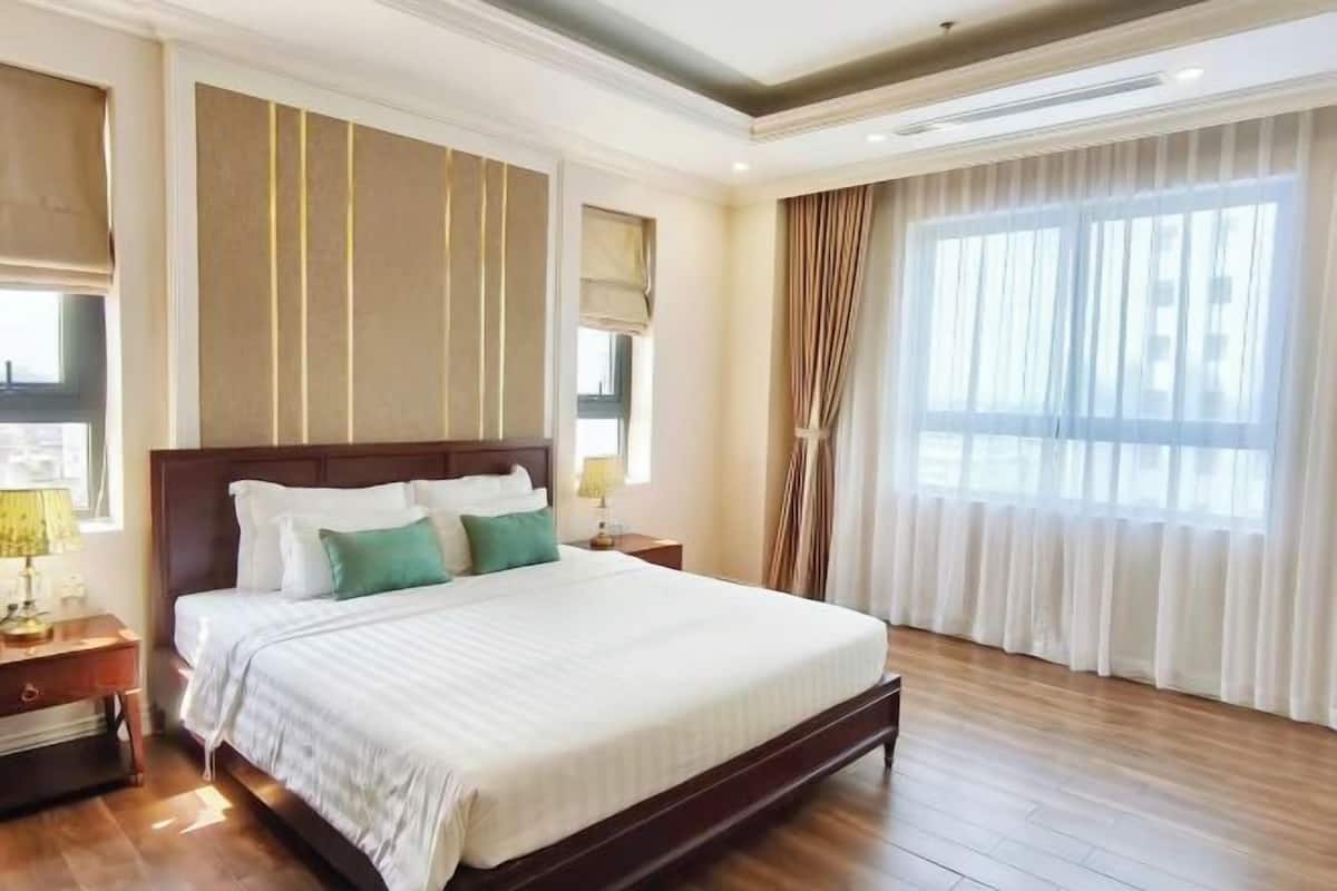 Une chambre d’hôtel avec un grand lit, un plancher en bois, une table de chevet avec une lampe et une fenêtre avec des rideaux.