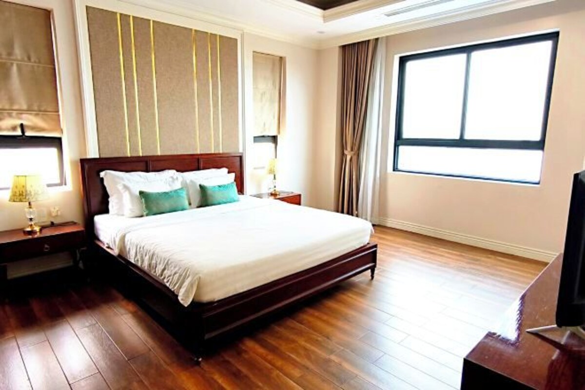A hotel room with a large bed, wooden flooring, a television, and a window with curtains.
