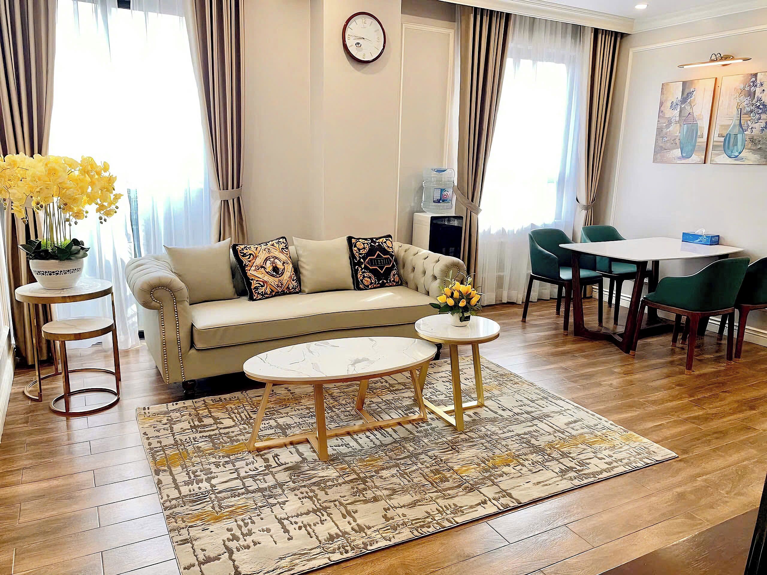 A living room with a sofa, two side tables, a coffee table, a dining table with chairs, and a clock on the wall.