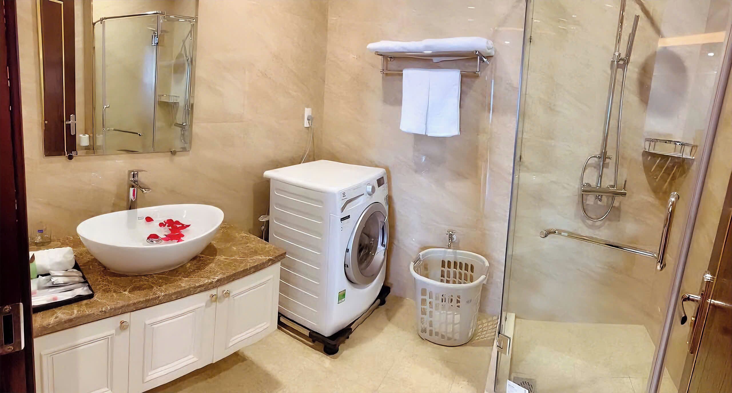 A bathroom with a sink, mirror, toilet, washing machine, and shower.