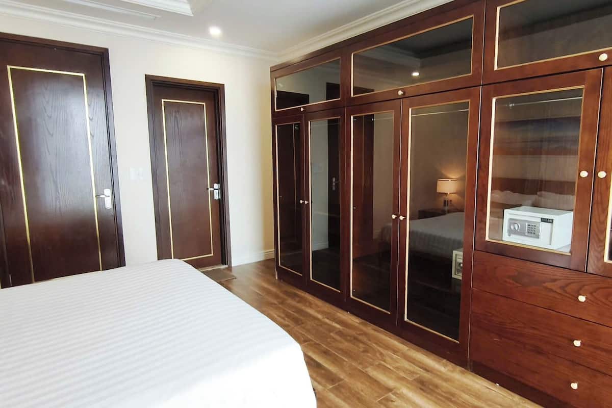 Une chambre d’hôtel avec un grand lit, une armoire en bois dotée de portes en verre et une petite table de chevet avec une lampe.