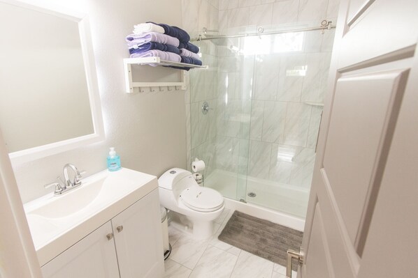 Un baño moderno con cabina de ducha de vidrio, lavabo blanco con espejo y retrete.
