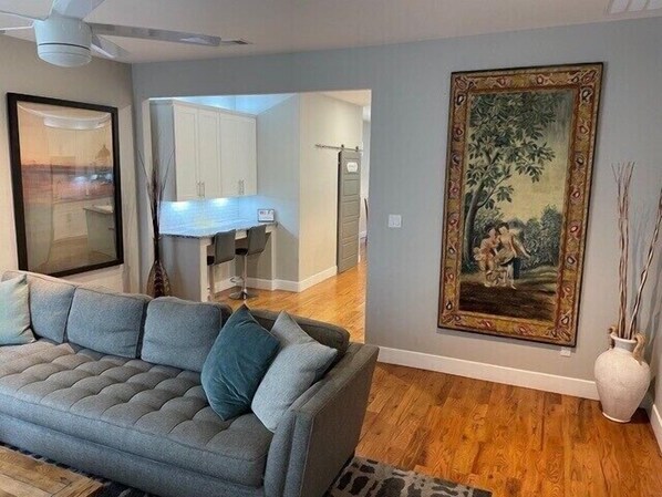 A living room with a grey sofa, a painting, and a vase on the wall.