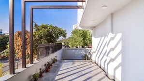 A modern building with a balcony, potted plants, and a clear view of the street and trees. - Royal Residence Golf View (Gurugram)