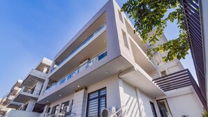 A modern multi-story building with balconies, large windows, and a staircase leading to the entrance. - Royal Residence Golf View (Gurugram)