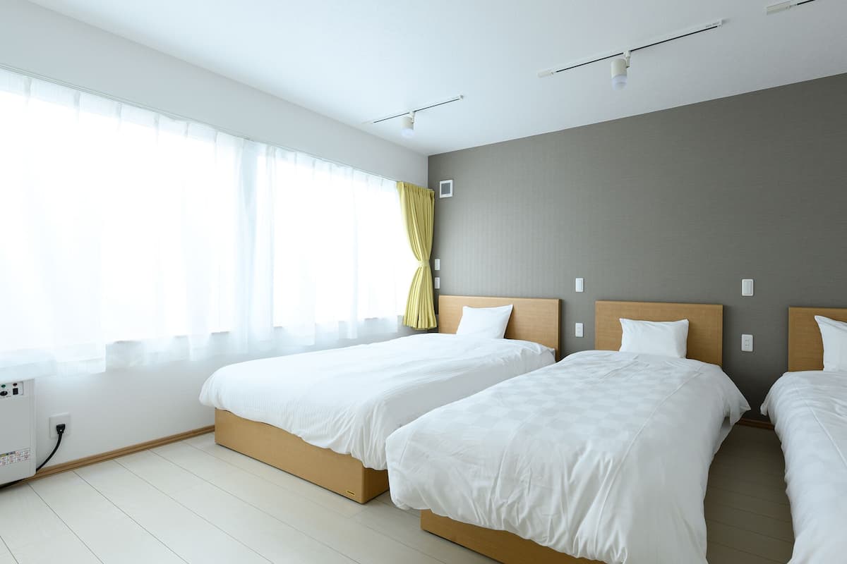 Ein Hotelzimmer mit zwei Betten, einem großen Fenster mit transparenten Vorhängen und einer neutralen Farbgestaltung.