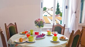 A dining table with breakfast items, including croissants, fruit, and beverages, set against a window with a view of buildings and a tree. - port view center city (Split)