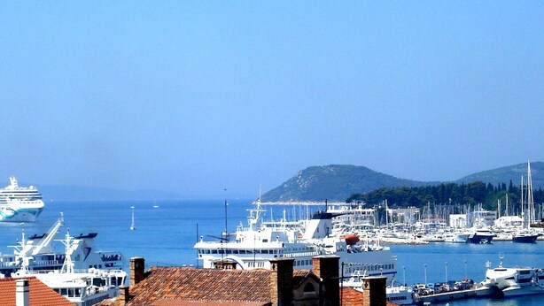 A marina with multiple boats docked, a cruise ship in the background, and a mountainous landscape. - port view center city (Split)