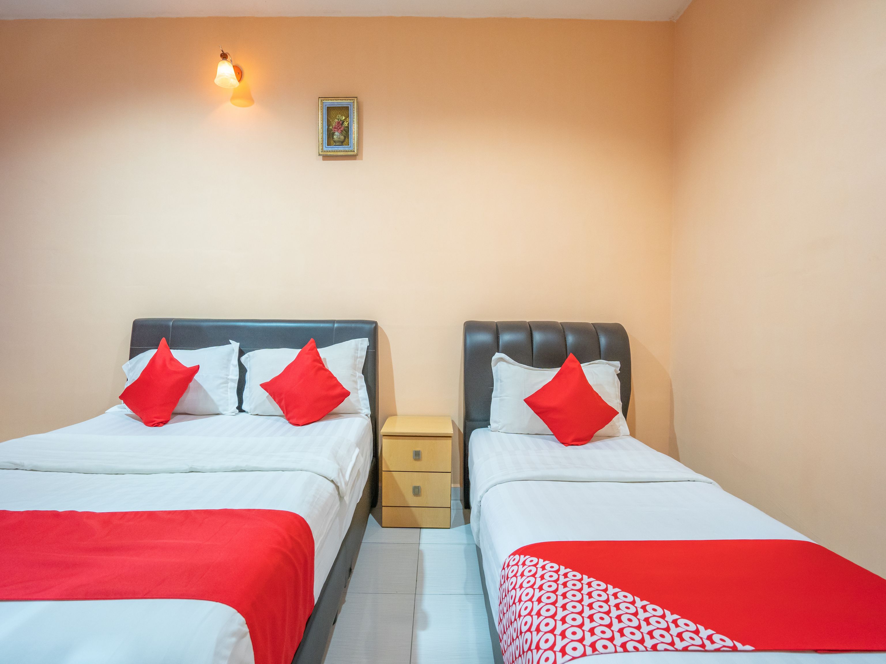 Habitación de hotel con dos camas, cada una con ropa de cama roja y blanca, una mesita de noche y una lámpara fijada a la pared.