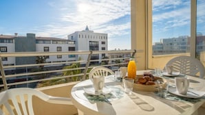 Ein Balkon mit Frühstückstisch, gedeckt mit Croissants und Orangensaft, mit Blick auf eine Skyline aus weißen Gebäuden.