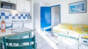 Eine moderne Küche mit weißen Schränken, einer Mikrowelle und einer gefliesten Spritzschutzwand. Es gibt einen Essbereich mit Tisch und Stühlen sowie eine blaue Tür, die zu einem weiteren Raum führt.