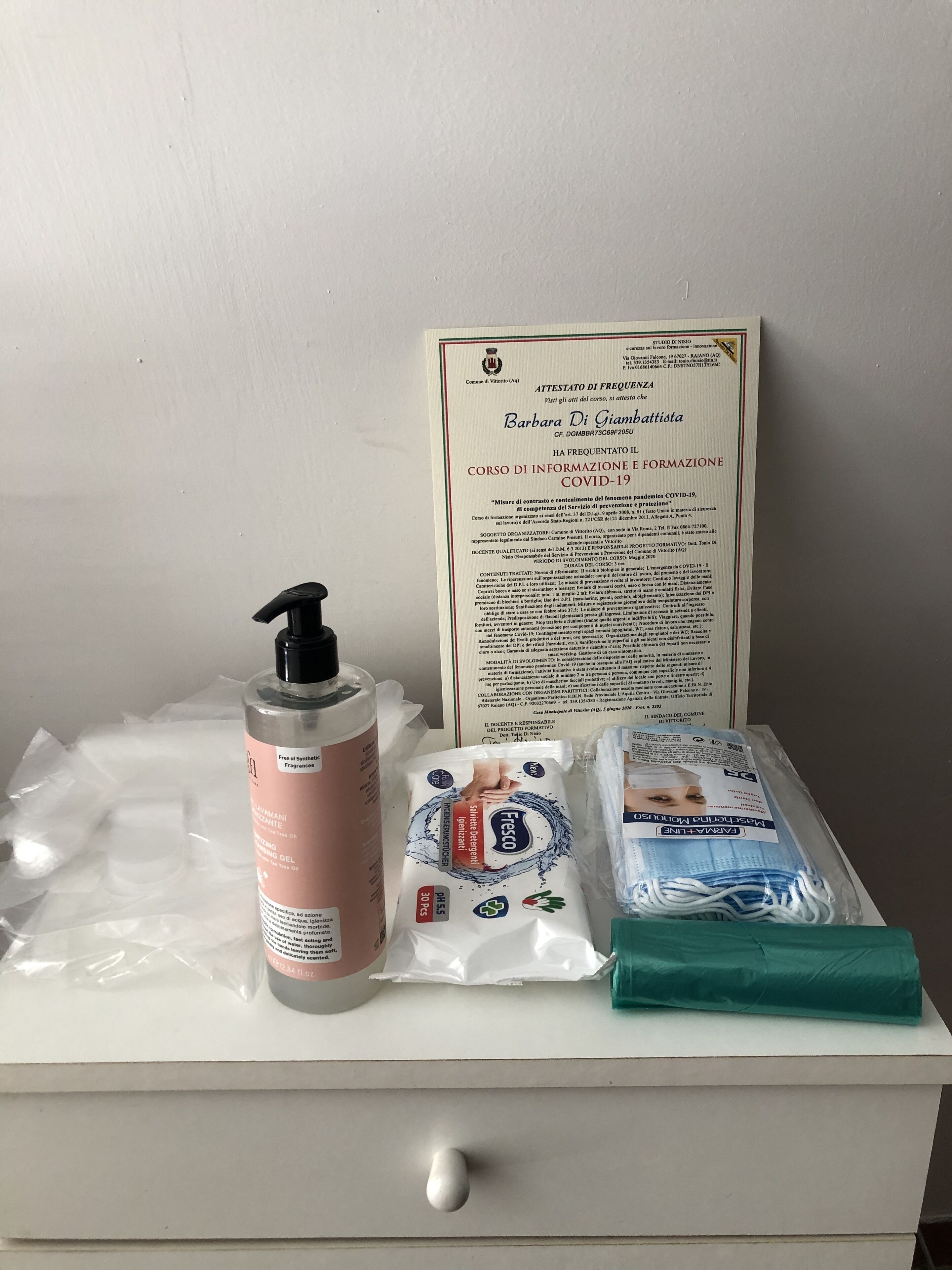Un comptoir de salle de bain avec un certificat, un flacon de gel hydroalcoolique, un paquet de mouchoirs et un masque facial vert.