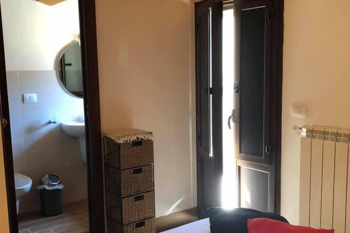 Un dormitorio con una cama, una almohada roja, techo de madera y una puerta que da al baño.