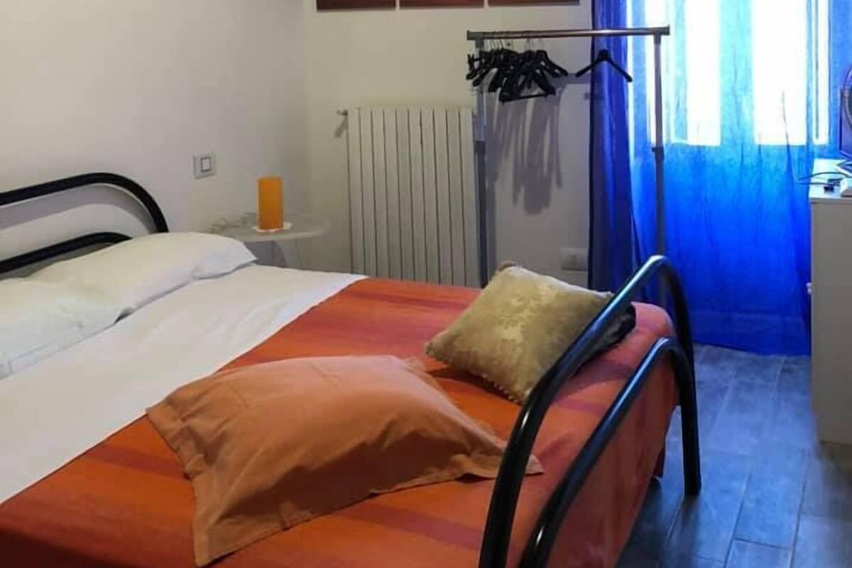 Un dormitorio con cama, radiador, una obra de arte en la pared, ventana con cortinas y escritorio con silla.