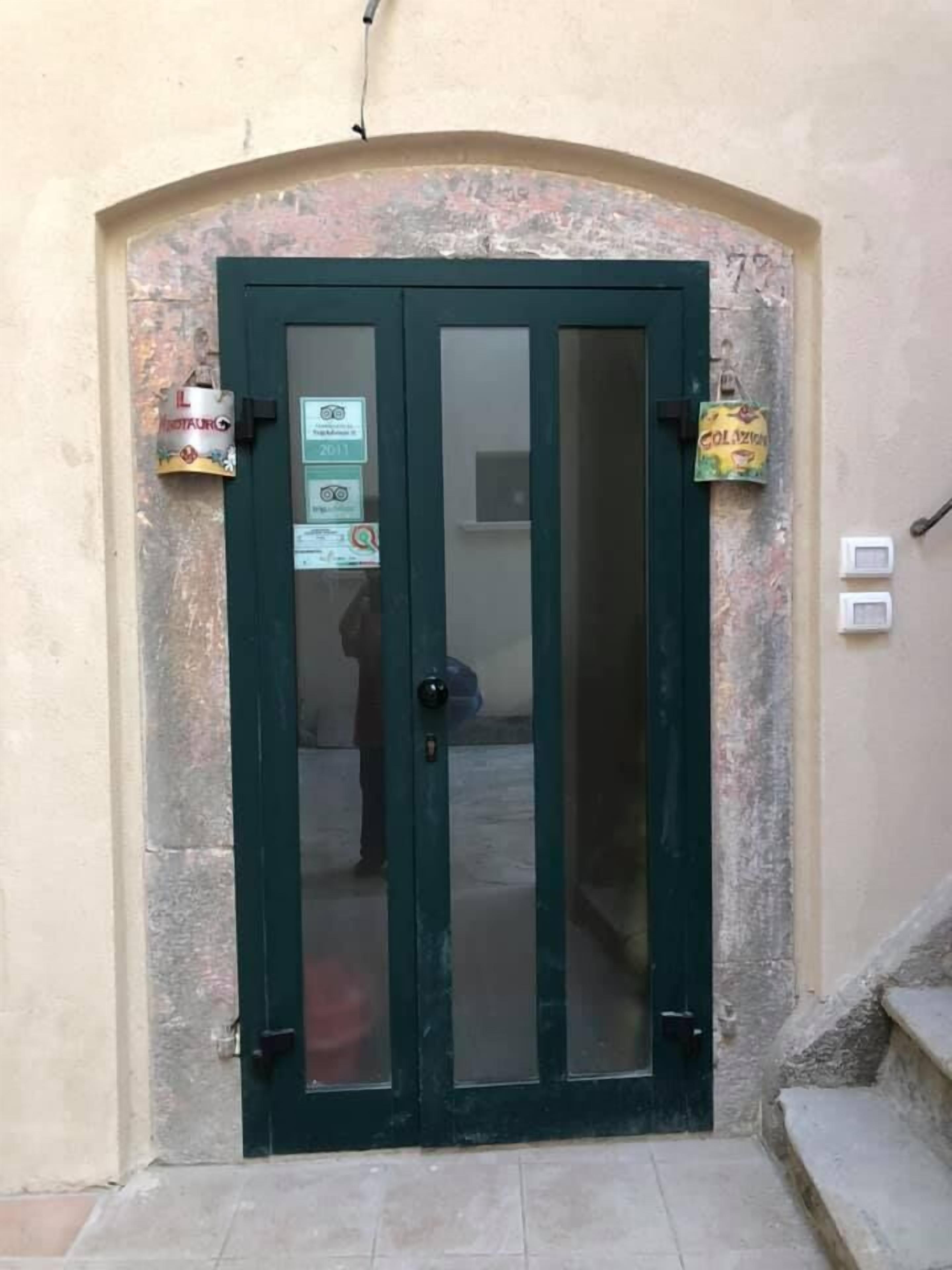 A dark green double door with a glass panel, a small sign on the left, and a bag hanging on the right.