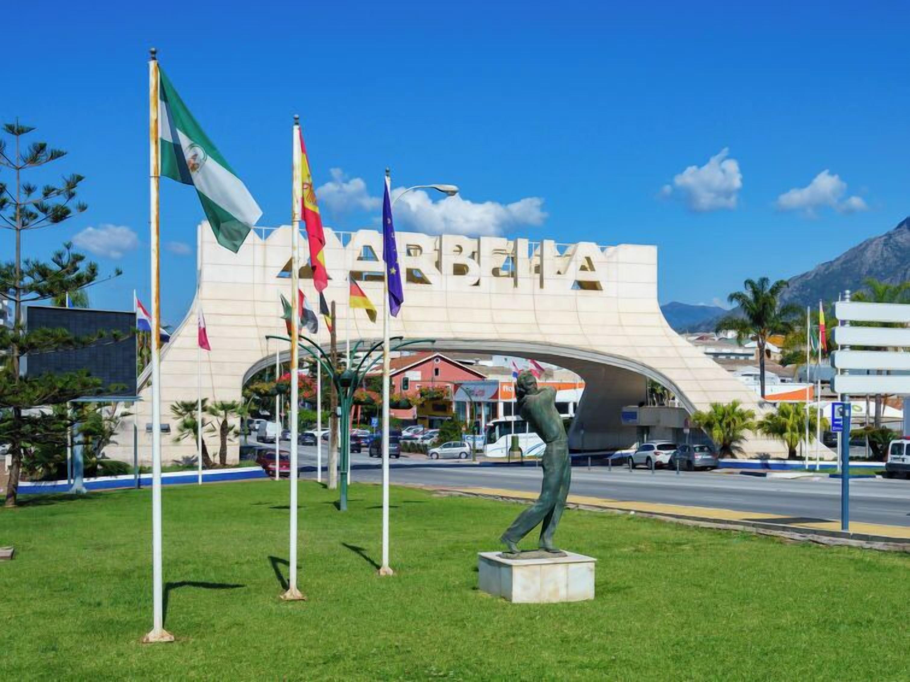 A building with the word "BARBIE" on its facade, surrounded by flags and a statue in a grassy area.