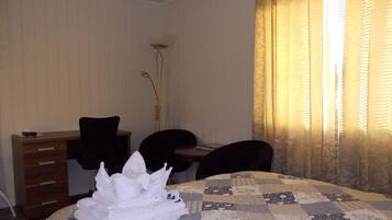 A hotel room with a bed, a desk, two chairs, a tall floor lamp, and a window with curtains.