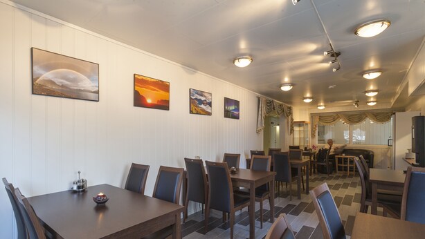 A restaurant with wooden tables and chairs, a tiled floor, and wall-mounted artwork. - Håkon Gjestehus (Kåfjord)