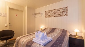 A hotel room with a bed, a chair, a wall-mounted air conditioner, and a decorative wall piece. - Håkon Gjestehus (Kåfjord)