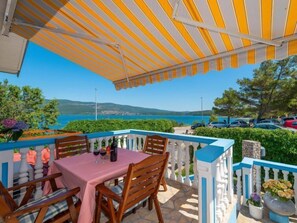 Un patio al aire libre con una mesa y sillas, vista al mar y coches aparcados.