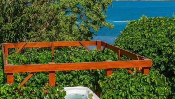 Un jacuzzi rodeado de exuberante vegetación y una terraza de madera, con vistas a un cuerpo de agua.