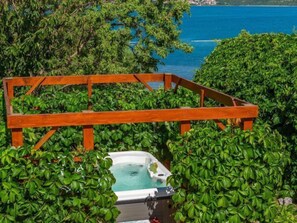A hot tub surrounded by lush greenery and a wooden deck, overlooking a body of water. - Vacation home Milka by Interhome (Novigrad (Zadar))