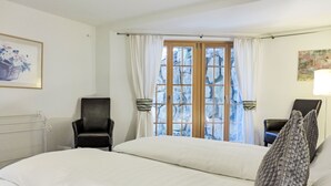 A hotel room with a large bed, two chairs, a window with curtains, and a painting on the wall.