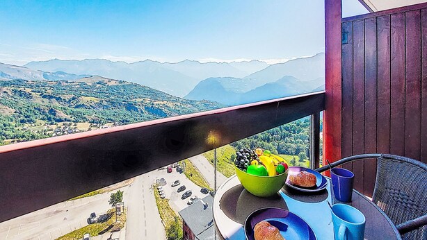 Un balcón con una mesa lista para el desayuno, un frutero y vistas a un paisaje montañoso.