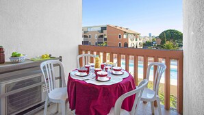 Un balcón con una mesa para dos, sillas blancas y un mantel rojo.