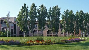 Un área ajardinada con césped, parterres de flores y un edificio con múltiples ventanas y balcones.